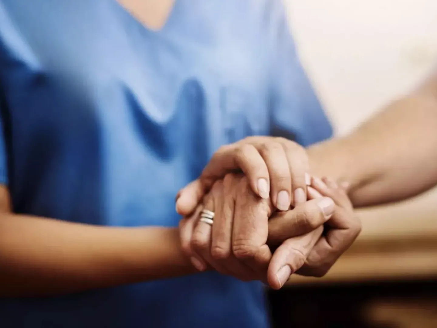 Close up of a healthcare professional holding hands with a patient to reassure them.